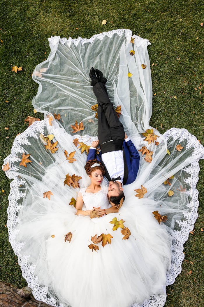 creative Bride and groom lying together on a lawn surrounded by autumn leaves, captured from above.