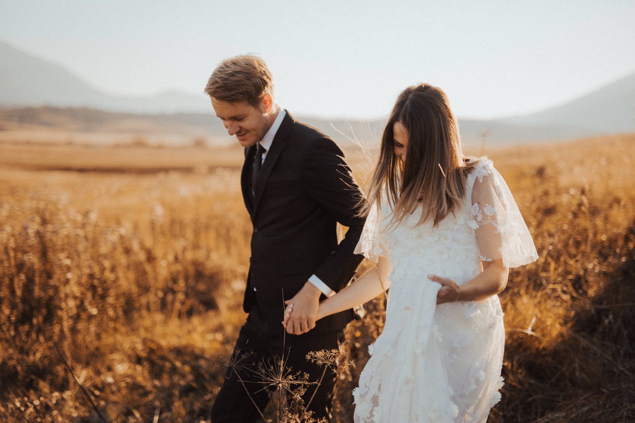 why-choose-us Newlywed couple walking hand in hand through a golden field on their wedding day, exuding love and happiness.