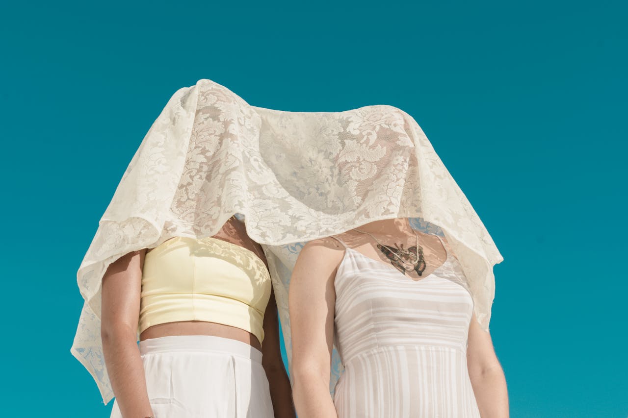 creative-03 Minimalist shot of two women under a white lace veil against a clear blue sky.