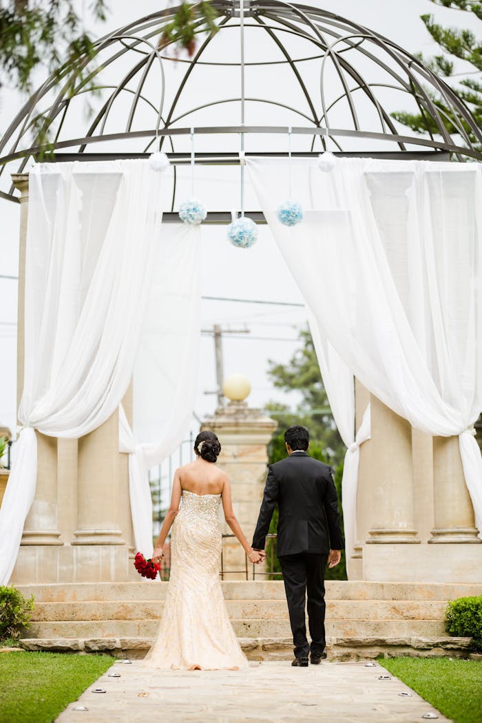 digital A couple holding hands, walking towards an elegant outdoor wedding arch in Marsfield, NSW.